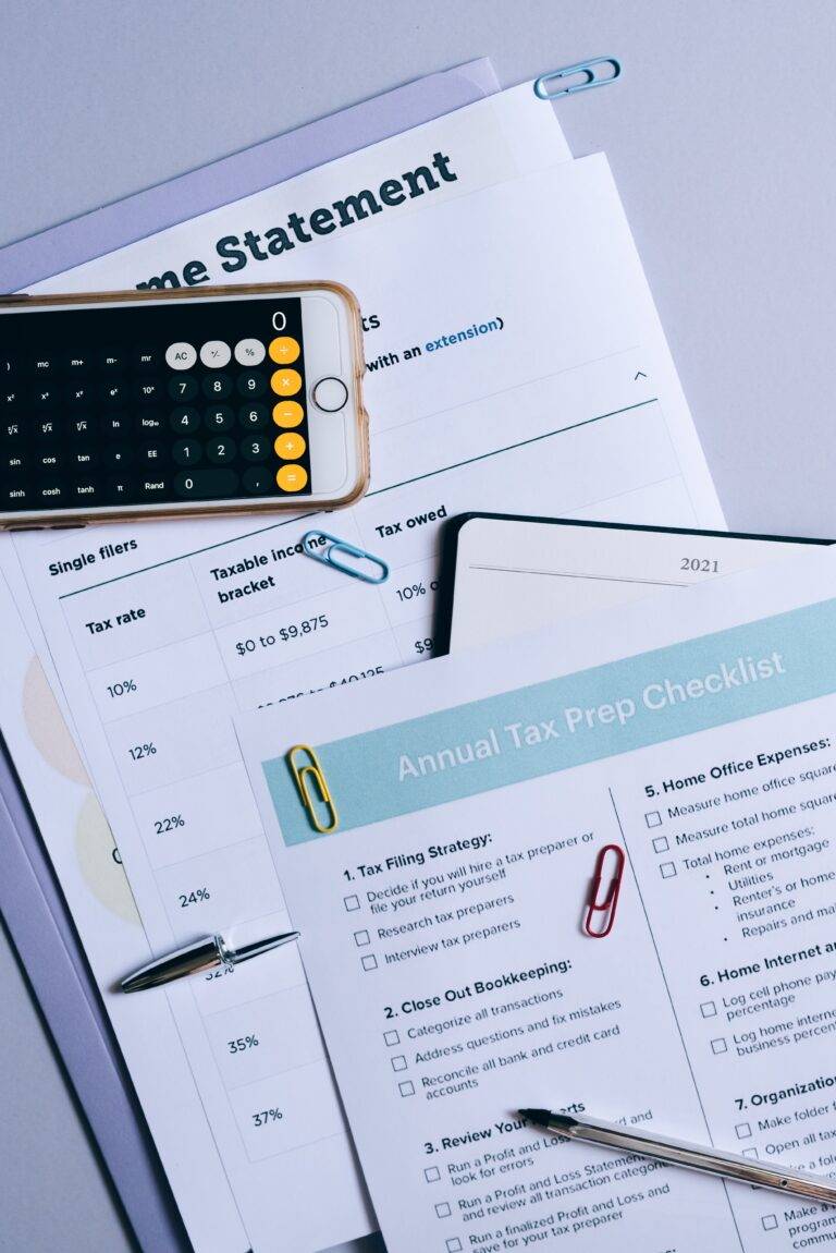 A photo of tax planning documents, including a tax rate sheet for single filers, a smartphone displaying a calculator app, and an 'Annual Tax Prep Checklist