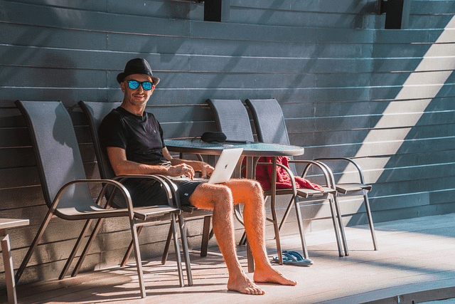 Homme portant des lunettes de soleil et une casquette, travaillant sur un ordinateur portable en plein air et recherchant le meilleur visa pour investir à Bali.